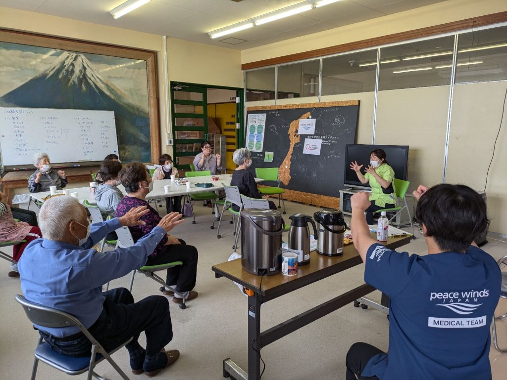 能登半島地震から1年半が経過。復旧・復興を支える支援レポート 7 健康相談会で座ったままのストレッチを行う参加者の写真